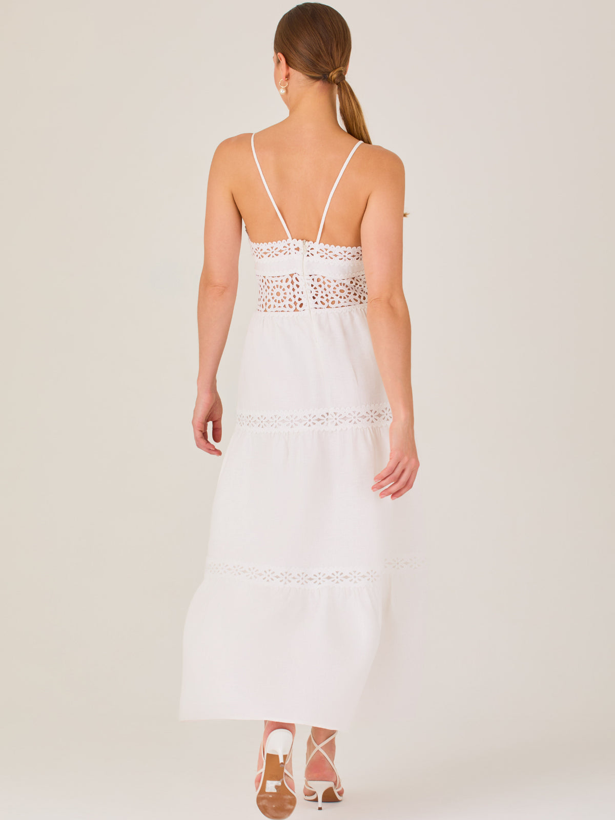 Este vestido largo blanco tiene un estilo fresco, romántico y veraniego. Cuenta con finos tirantes y un escote en “V” pronunciado, delicadamente adornado con bordado tipo encaje floral que continúa en la cintura, generando un efecto de transparencia sutil y elegante.

La falda de corte amplio y largo midi cae suavemente desde la cintura, con detalles de franjas horizontales de bordado calado que repiten el motivo floral. El tejido ligero y vaporoso aporta comodidad y libertad de movimiento.