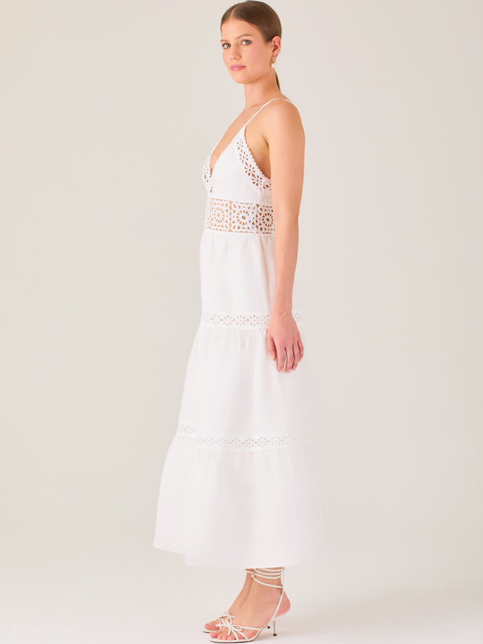 Este vestido largo blanco tiene un estilo fresco, romántico y veraniego. Cuenta con finos tirantes y un escote en “V” pronunciado, delicadamente adornado con bordado tipo encaje floral que continúa en la cintura, generando un efecto de transparencia sutil y elegante.

La falda de corte amplio y largo midi cae suavemente desde la cintura, con detalles de franjas horizontales de bordado calado que repiten el motivo floral. El tejido ligero y vaporoso aporta comodidad y libertad de movimiento.