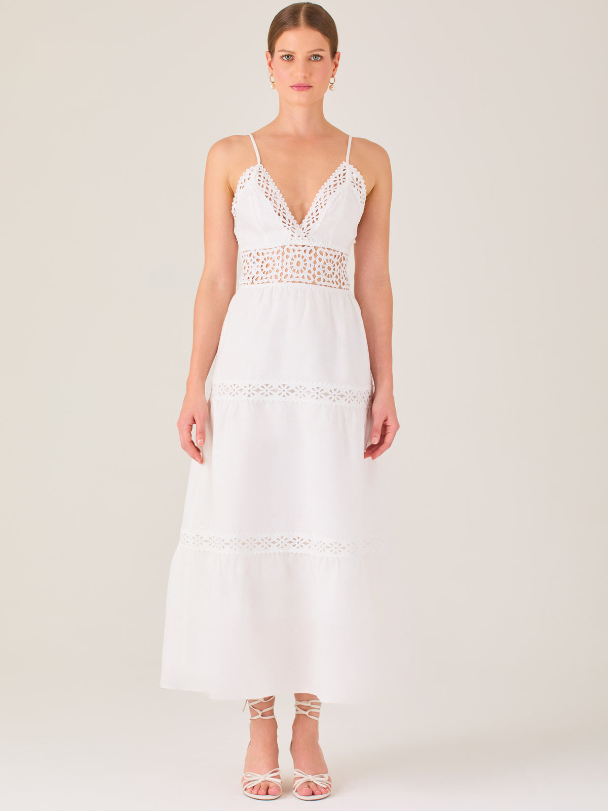 Este vestido largo blanco tiene un estilo fresco, romántico y veraniego. Cuenta con finos tirantes y un escote en “V” pronunciado, delicadamente adornado con bordado tipo encaje floral que continúa en la cintura, generando un efecto de transparencia sutil y elegante.

La falda de corte amplio y largo midi cae suavemente desde la cintura, con detalles de franjas horizontales de bordado calado que repiten el motivo floral. El tejido ligero y vaporoso aporta comodidad y libertad de movimiento.