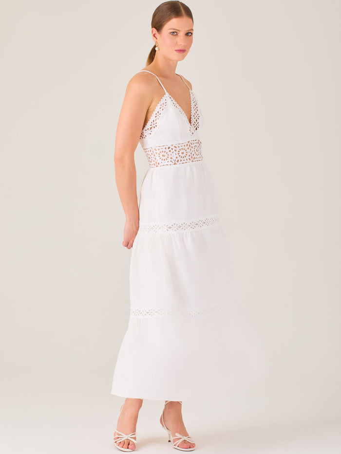 Este vestido largo blanco tiene un estilo fresco, romántico y veraniego. Cuenta con finos tirantes y un escote en “V” pronunciado, delicadamente adornado con bordado tipo encaje floral que continúa en la cintura, generando un efecto de transparencia sutil y elegante.

La falda de corte amplio y largo midi cae suavemente desde la cintura, con detalles de franjas horizontales de bordado calado que repiten el motivo floral. El tejido ligero y vaporoso aporta comodidad y libertad de movimiento.